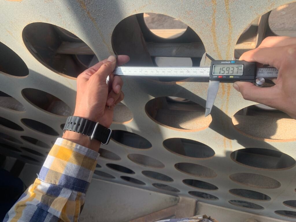 Digital caliper measuring a cut-out hole diameter on a bag filter tube sheet during inspection